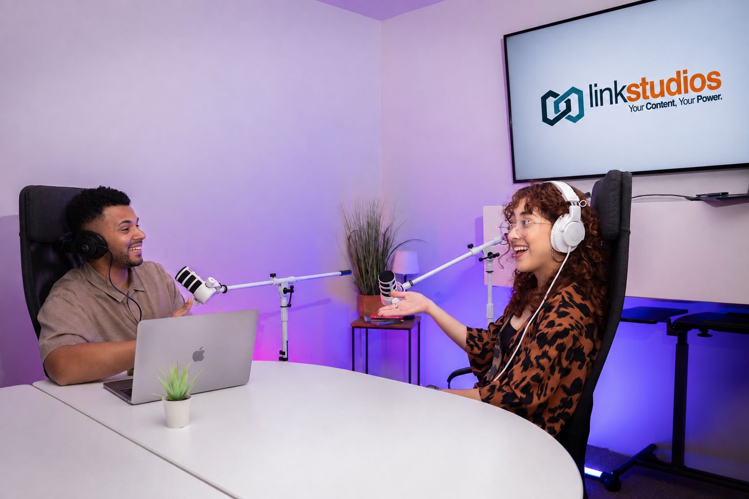 Grabación de podcast en Link Studios con dos personas, micrófonos de brazo y pantalla con el logo Link Studios